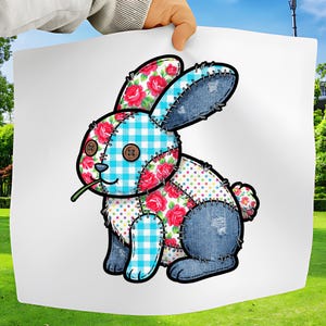 Op de afbeelding: Een patchwork konijn illustratie met een grillig ontwerp. Het konijn heeft denim, bloemen en gingham patronen, met knoopogen en een groene stengel in zijn mond. Het ontwerp is aan elkaar gestikt met zichtbaar draad.