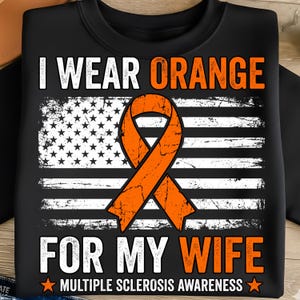 May include: Black t-shirt with the text "I WEAR ORANGE FOR MY WIFE" and "MULTIPLE SCLEROSIS AWARENESS". The design includes an orange awareness ribbon over a distressed American flag.