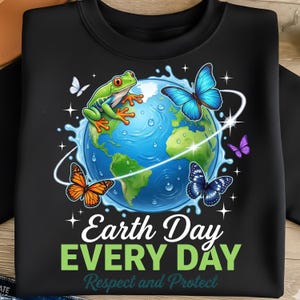 Peut inclure: T-shirt noir avec un motif coloré représentant la Terre, une grenouille, des papillons et le texte "Earth Day EVERY DAY Respect and Protect". Le design comprend un globe bleu et des continents verts.