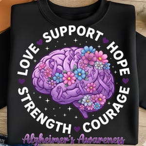Può includere: Felpa nera con grafica di un cervello viola, ornata da nastri viola e fiori colorati. Il design include le parole "Love, Support, Hope, Courage, Strength" e "Alzheimer's Awareness."