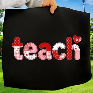 Może przedstawiać: Czarna torba z napisem "teach" w stylu patchwork. Litery są w odcieniach czerwieni, różu i bieli, z wzorami kwiatowymi i w kropki. Zawiera akcent w kształcie serca.