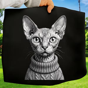 May include: Black fabric featuring a detailed illustration of a Sphynx cat wearing a cable-knit sweater. The cat has large, expressive eyes and prominent ears. The artwork is in black and white, with intricate shading and texture.