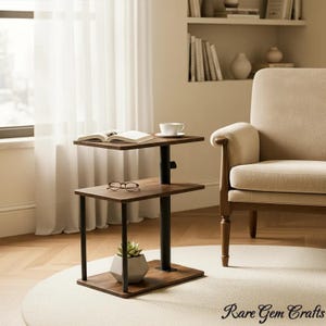 May include: A two-tiered, dark wood side table with a black central support. The top tier holds a book and a teacup, while the bottom tier has eyeglasses and a small potted plant. The table is on a cream-colored rug.