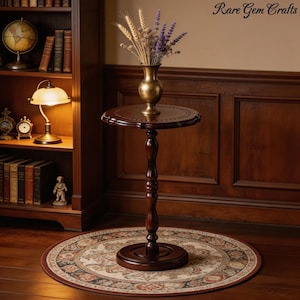 May include: A dark brown, antique-style plant stand with a round top and base. The stand features a decorative, turned central column. A gold-colored vase with dried flowers sits on top. The stand is placed on a patterned rug.