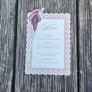 Op de afbeelding: Een rechthoekige menukaart met een geschulpte, kanten rand in oudroze. De kaart bevat een illustratie van een donkerpaarse calla-lelie met de naam William op het bloemblad. De tekst vermeldt de gangen Entree, Plat en Dessert.