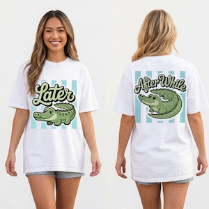 Könnte beinhalten: Weißes T-Shirt mit einem grünen Cartoon-Alligator und dem Wort "Later" in Schreibschrift. Auf der Rückseite des Shirts stehen die Worte "After While" und ein ähnliches Alligatordesign. Hellblaue vertikale Streifen befinden sich hinter den Designs.