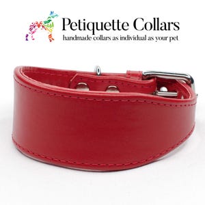 Op de afbeelding: Een rode leren hondenriem met een zilveren gesp en stiksels. De riem is handgemaakt en heeft een breed, plat ontwerp.