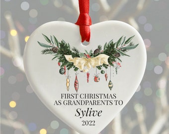 Peut inclure: Ornement de Noël en céramique blanc en forme de cœur avec une couronne verte et dorée, des baies rouges et un nœud. L'ornement porte l'inscription "Premier Noël en tant que grands-parents de Sylvie 2022".