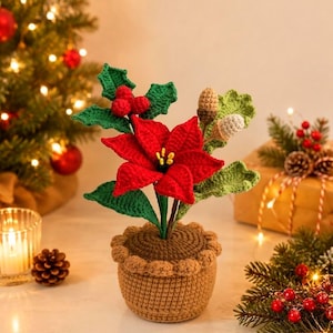 May include: A crocheted poinsettia plant in a brown pot with a scalloped rim. The plant features vibrant red petals with yellow centers, green holly leaves, red berries, and two small acorns. The entire arrangement is crafted from yarn.