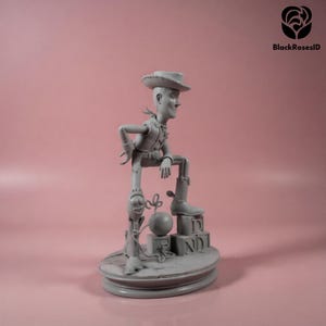K&ouml;nnte beinhalten: Graue Figur eines Cowboy-Charakters, der einen Hut, eine Weste und Stiefel tr&auml;gt und sich auf Holzbl&ouml;cken abst&uuml;tzt. Eine Bombe und ein Seil sind ebenfalls vorhanden. Die Figur steht auf einem runden Sockel. Der Hintergrund ist einfarbig rosa.