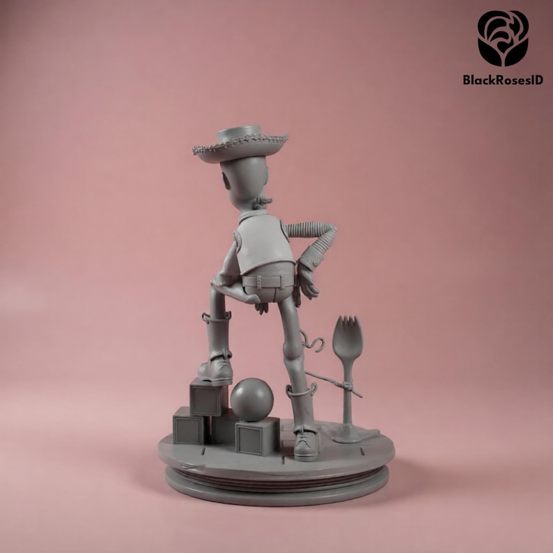 K&ouml;nnte beinhalten: Graue Figur eines Cowboy-Charakters, der einen Hut, eine Weste und Stiefel tr&auml;gt, steht auf einer Plattform mit geometrischen Formen. Ein l&ouml;ffelartiges Objekt ist an der Basis befestigt. Die Figur posiert mit einem Bein nach oben.