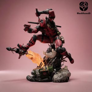 May include: A detailed Deadpool action figure in a dynamic leaping pose, wearing a red and black suit with utility belts. The character holds a handgun and a katana, positioned above a base featuring a green barrel with the text BOOM and fire effects.