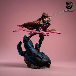 Può includere: Una dettagliata statuetta da collezione di un personaggio con capelli castani, che indossa un trench marrone sopra una tuta blu e magenta. La figura poggia su una grande mano meccanica blu, impugnando un bastone argentato e un effetto energetico rosa.
