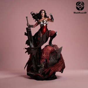 May include: A detailed figurine of a warrior with long dark hair, wearing a metallic silver and red bodice, dark pants, and arm guards. The figure holds a large, heavy sword and stands atop a textured, red dragon-like creature on a rocky base.
