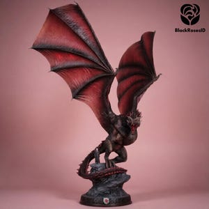 May include: A detailed dragon statue with outstretched wings, featuring a dark body and vibrant red wings. The dragon is perched on a rocky base, with a detailed tail and open mouth. The statue has a dark base with a crest.