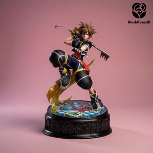 May include: A detailed figurine of a character from the Kingdom Hearts video game series. The figure is posed dynamically, holding a key-shaped weapon. The base features a stained-glass design. The character wears a black, blue, and yellow outfit.
