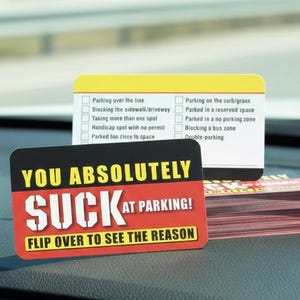 Könnte beinhalten: Ein Stapel rot-weißer Karten mit dem Text "YOU ABSOLUTELY SUCK AT PARKING! FLIP OVER TO SEE THE REASON" auf der Vorderseite. Eine gelb-weiße Karte mit Parkverstoßoptionen befindet sich dahinter.