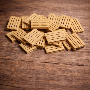 Può includere: Un gruppo di piccoli bancali in legno marrone chiaro sparsi su una superficie di legno. I bancali sono rettangolari con doghe orizzontali, e la venatura del legno è visibile. Lo sfondo è di una tonalità marrone più scura.