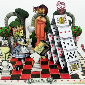 May include: A 3D papercraft scene depicting characters from Alice in Wonderland. Alice stands on a checkered board with a Queen, two Cheshire Cats, and a Mad Hatter. A house of cards stands in the background with the White Rabbit holding a pocket watch.
