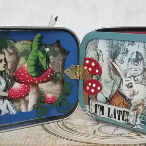 May include: Two vintage tin boxes with a whimsical Alice in Wonderland theme. The left box features a blue background with a cutout of Alice and a mushroom. The right box features a blue background with a cutout of the Mad Hatter and the March Hare. Both boxes have the text "I'm Late!" on the front.