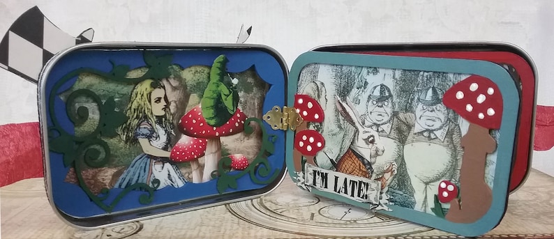 May include: Two vintage tin boxes with a whimsical Alice in Wonderland theme. The left box features a blue background with a cutout of Alice and a mushroom. The right box features a blue background with a cutout of the Mad Hatter and the March Hare. Both boxes have the text "I'm Late!" on the front.