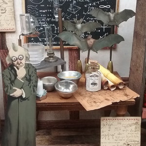 May include: A miniature scene of a scientist's workspace with a chalkboard filled with mathematical equations, a glass beaker, a small bottle with a cork stopper, and a figurine of a scientist wearing a green coat and glasses. There are also several scrolls and small bowls on a wooden table.