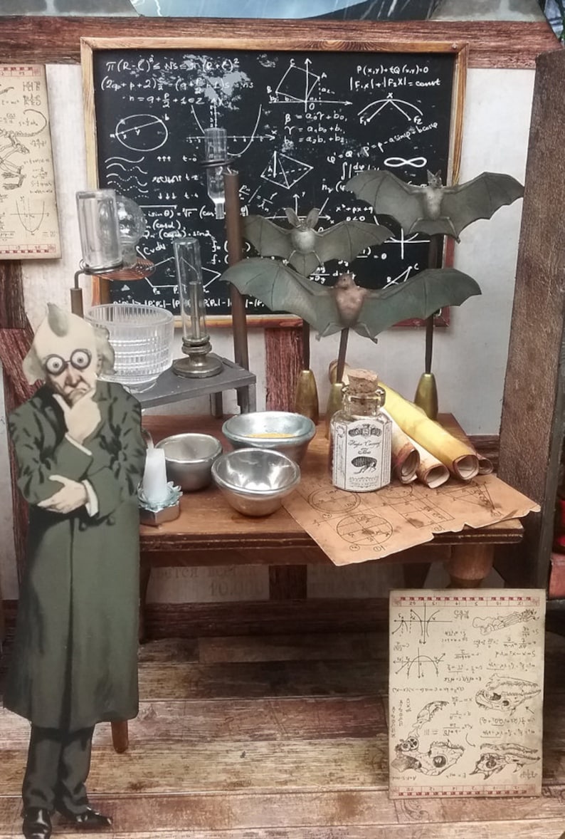 May include: A miniature scene of a scientist's workspace with a chalkboard filled with mathematical equations, a glass beaker, a small bottle with a cork stopper, and a figurine of a scientist wearing a green coat and glasses. There are also several scrolls and small bowls on a wooden table.
