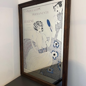 Peut inclure: Un miroir mural rectangulaire avec un cadre en bois foncé présentant une impression graphique de style vintage. L'illustration montre une personne tenant un miroir à main bleu, avec le texte L'ONDULATION PERMANENTE, EUGÈNE et 23 Grafton Street LONDON.