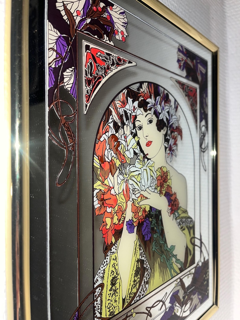 May include: Art Nouveau style framed print featuring a woman with flowers. The artwork has a gold frame and a color palette of red, yellow, purple, and green. The woman is holding a bouquet of flowers.