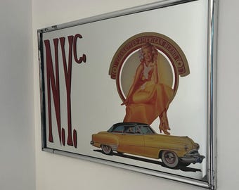May include: A rectangular wall mirror with a chrome frame featuring a graphic print. The design includes the red text N.Y.C., a circular emblem with the text CIGARETTES AMERICAN BLEND, a seated figure in a yellow dress, and a yellow vintage car.