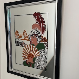 Peut inclure: Un miroir mural rectangulaire avec un cadre noir et une bordure intérieure argentée. La vitre présente une illustration graphique d'une personne avec une coiffe à plumes, tenant un éventail, vêtue d'un vêtement vert, avec une voiture ancienne.