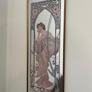 Peut inclure: Un miroir mural rectangulaire doté d'un cadre décoratif avec une illustration imprimée d'une personne en robe rose fluide, le menton posé sur la main. L'œuvre présente des motifs floraux et des lignes arquées dans des tons rose et brun.