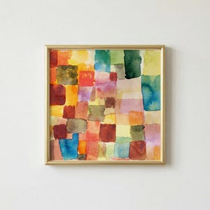 Op de afbeelding: Vierkant ingelijst aquarel schilderij met een gouden lijst. Het kunstwerk toont een raster van kleurrijke, onregelmatige vierkanten in tinten rood, oranje, geel, groen, blauw en paars. Het schilderij heeft een textuur, abstract uiterlijk.
