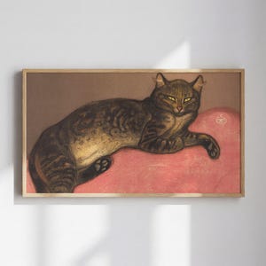 Puede incluir: Obra de arte enmarcada que presenta un gato atigrado descansando sobre un cojín rosa. El gato tiene ojos amarillos y un pelaje marrón y dorado. El fondo es marrón apagado y el marco es de madera clara.