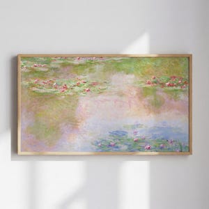 Op de afbeelding: Een ingelijste kunstdruk van een waterlelievijver. Het schilderij toont zachte penseelstreken in tinten groen, roze en blauw, die waterlelies en bloemen afbeelden die op het wateroppervlak drijven. Het kunstwerk zit in een houten lijst.