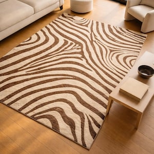 Op de afbeelding: Een rechthoekig vloerkleed met een zebra streepmotief in bruin en beige. Het kleed ligt op een houten vloer in een woonkamer, met een bank, fauteuil en salontafel.