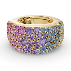 May include: A wide gold band ring featuring a dense pavé setting of round faceted gemstones in a gradient color scheme. The stones transition from pink on the left to purple in the center, and light blue to turquoise on the right side.