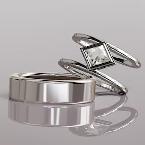 May include: A set of two silver-toned rings. One ring is a wide, smooth, polished band with a flat profile. The second ring features a bypass design with a square-cut clear gemstone set in a dark, square-shaped bezel at the center point.