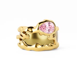 May include: A gold ring featuring an irregular, organic, molten-style band with a smooth, polished finish. A single pear-shaped, light pink gemstone is set prominently within the upper section of the gold metal structure.