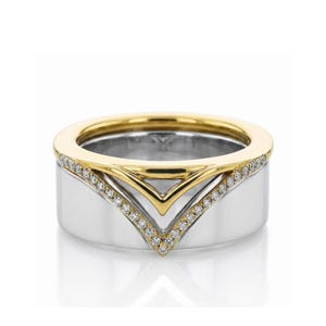 May include: A wide band ring featuring a polished silver-tone base and a contrasting gold-tone top section. The ring is accented with a V-shaped inlay of small, clear pavé-set stones that follow the chevron contour where the two metal colors meet.