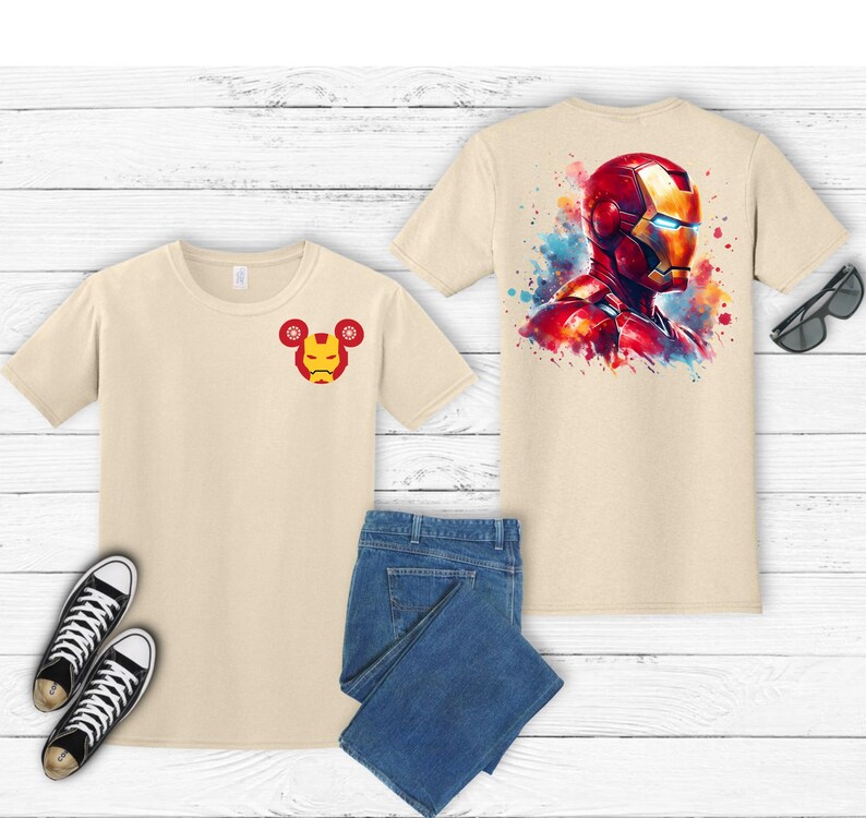 Puede incluir: Dos camisetas beige con dise&ntilde;os de Iron Man, una en la parte delantera y otra en la trasera. El dise&ntilde;o delantero es una peque&ntilde;a cara de Iron Man. El dise&ntilde;o trasero es una cabeza de Iron Man al estilo acuarela. La imagen tambi&eacute;n incluye vaqueros azules y zapatillas negras.