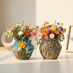 Puede incluir: Dos jarrones decorativos llenos de flores coloridas. Uno es azul con un diseño de girasol, y el otro es de color bronce con un patrón de sol y floral. Los jarrones están sobre una superficie blanca.