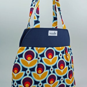 May include: A navy blue tote bag with a yellow, red, and purple floral pattern. The bag has a navy blue flap with the text "annika in Copenhagen" on a white label.
