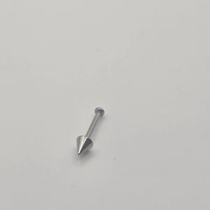 May include: A silver-colored, pointed stud earring. The earring has a conical, sharp end and a small, round backing. The jewelry is set against a plain, light background.