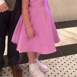 May include: A light pink dress with a sparkling strap and a flared skirt. The dress is paired with white sneakers adorned with pink embellishments. The image captures a formal or celebratory occasion.