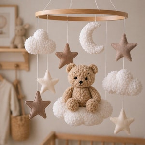Pode incluir: Móvel de berço com um urso de pelúcia, estrelas, nuvens e uma lua crescente suspensos em um anel de madeira. Os brinquedos macios são em tons neutros, criando uma decoração relaxante para o quarto do bebê.