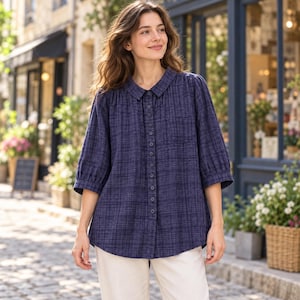 May include: A dark blue button-down shirt with a subtle crosshatch pattern, featuring a classic collar, three-quarter length sleeves with gathered cuffs, and a single chest pocket, paired with light-colored trousers in a relaxed fit.