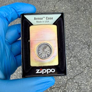May include: A Zippo Armor Case lighter with a brass finish and a Native American chief skull design. The lighter is in its original black box, with the text "Armor Case Made in USA".