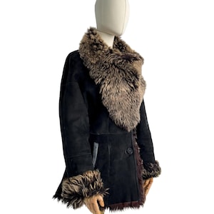 May include: A black shearling coat with a large, brown fur collar and cuffs. The coat has a single button closure and a tailored fit. The fur trim adds a luxurious touch to this outerwear piece.