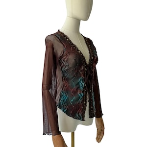 May include: A long-sleeved, sheer mesh top in deep brown featuring a V-neckline with a front tie closure. The garment is decorated with vertical, wavy, multi-colored patterns in shades of teal, rust, and brown, accented with small, dark sequins.
